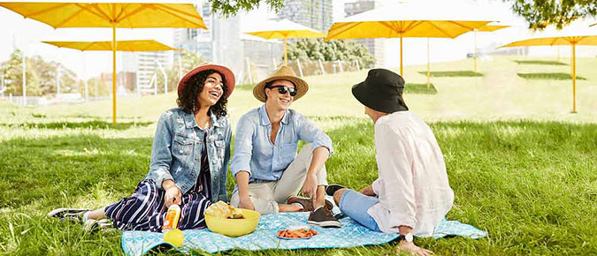 Group of people sitting on picnic mat in the park. 