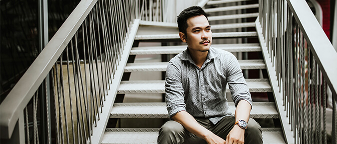 Asian man sitting on the stairs looking away.