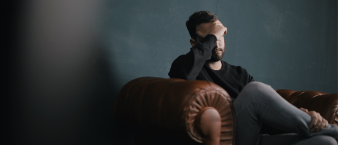 Sad man seated on the couch with his hands on his head.