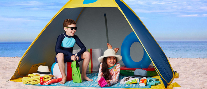 Two children sitting in a tent on the beach.