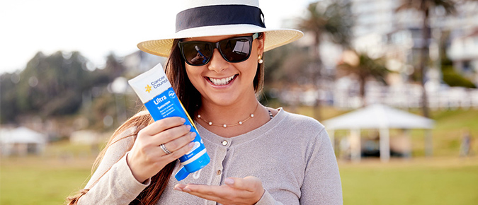 Woman wearing sunglasses applying sunscreen.