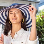 Woman wearing a hat and holding sunscreen.