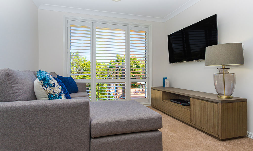 A lounge room with a couch, entertainment unit, lamp and flat screen TV