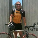 A man standing with a bicycle at the NSW-QLD border.