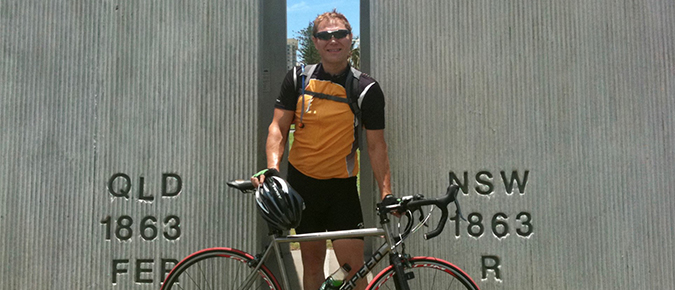 A man standing with a bicycle at the NSW-QLD border. 
