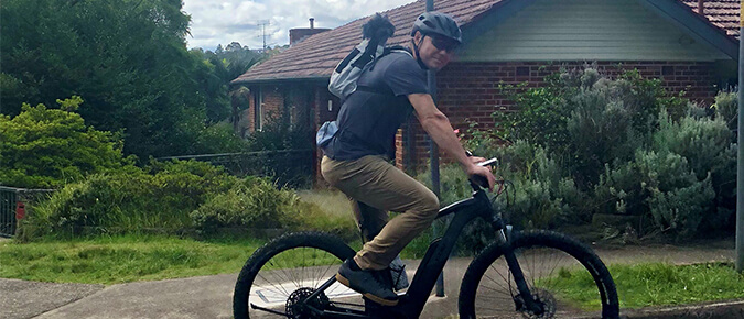 Man riding bicycle with a dog on his back.