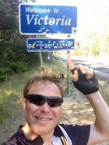 Man pointing to a sign saying 'Welcome to Victoria'