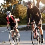 A man and woman wearing helmets cycling on a road.