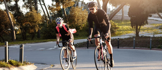 A man and woman wearing helmets cycling on a road.
