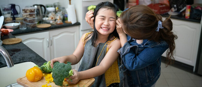 Asian mother holding broccoli against little girl's face.