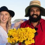 Young Caucasian woman and Indigenous man at the beach holding daffodils.