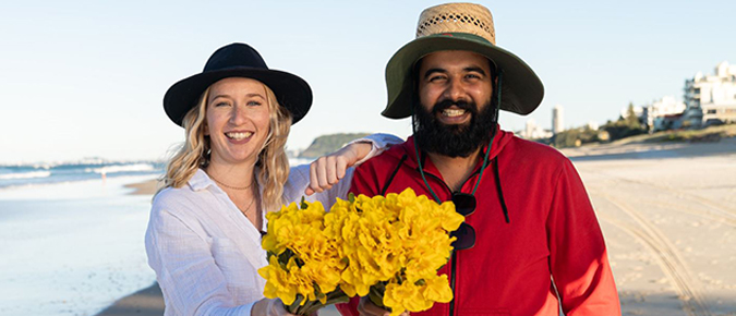 Young Caucasian woman and Indigenous man at the beach holding daffodils.