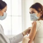 Masked doctor giving vaccination to young woman wearing mask.