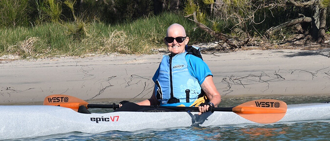 Bald woman wearing sunglasses on a kayak.