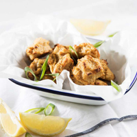 Cauliflower nuggets prepared in an air fryer served in a white bowl with garnishes and slices of lemon 