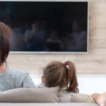 The back of three children on the sofa looking at a television.