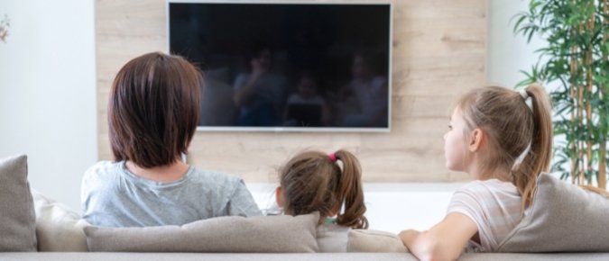 The back of three children on the sofa looking at a television.