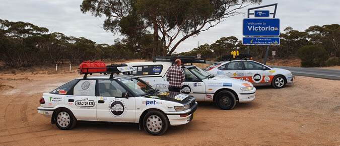 Three cars parked on a dirt road. 