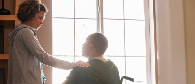 Woman with her hand on shoulder of man in a wheelchair.