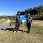 Two golfer at Northbridge Golf Club holding a sign saying "It's never too late to reduce your risk of melanoma".