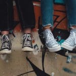 Young people dangling feet in front of a graffitied wall