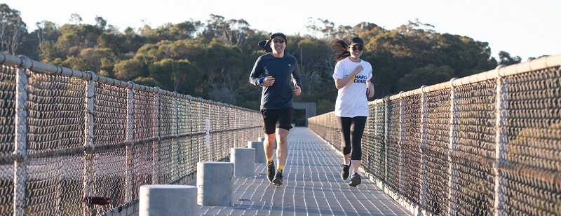 man and woman running on a bridge for the cancer council march charge 2023