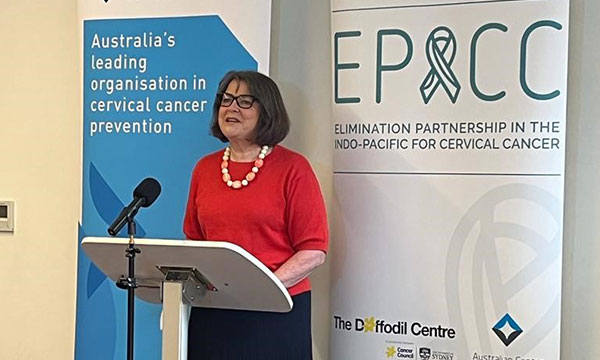 A researcher speaks in front of a Daffodil Centre banner reading 'Elimination Partnership in the Indo-Pacific for the Elimination of Cervical Cancer' 