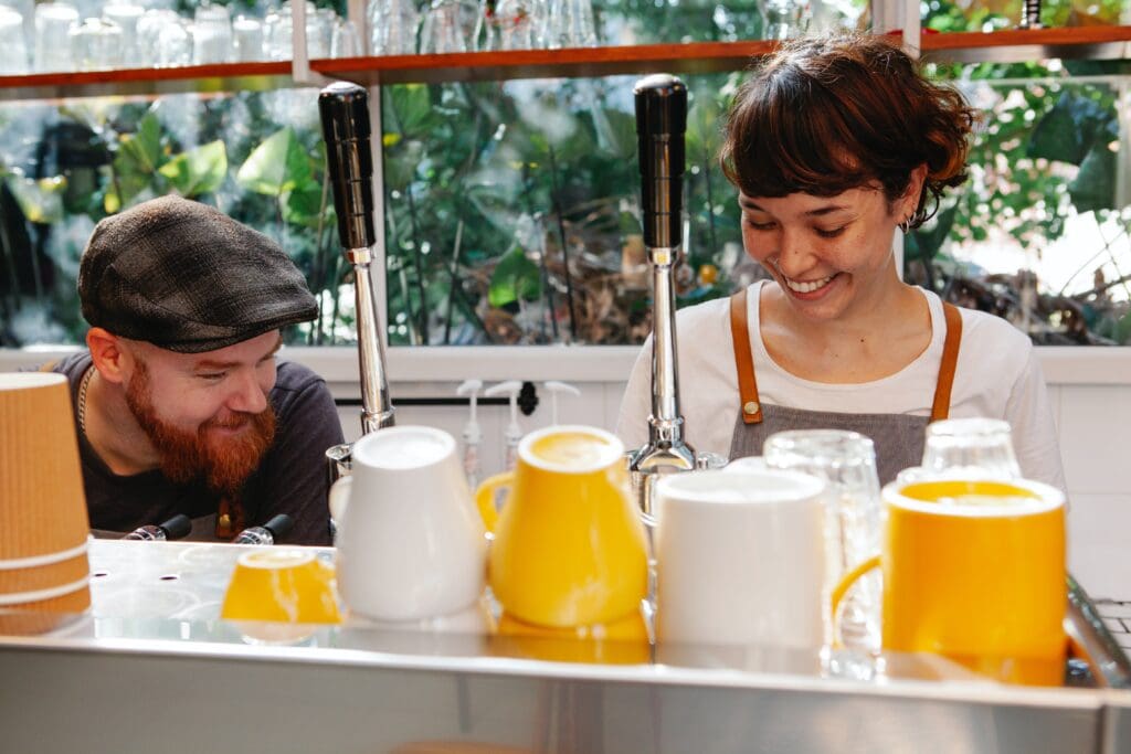 A photo of two co-workers in a cafe, smiling as they do their work.
