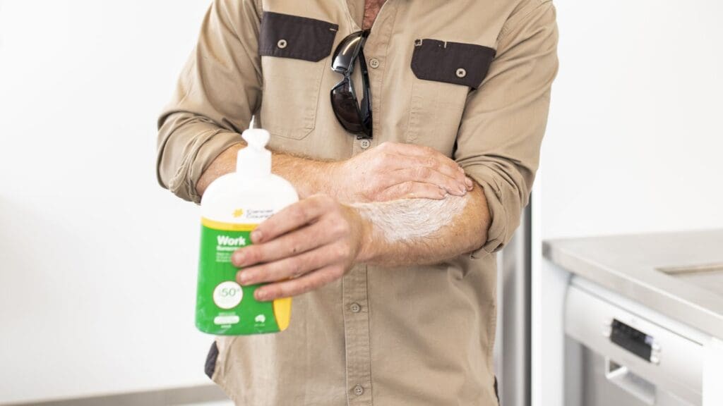 Photo of an outdoor worker in a common area at work. They are putting on Cancer Council NSW Work Sunscreen SPF 50+.