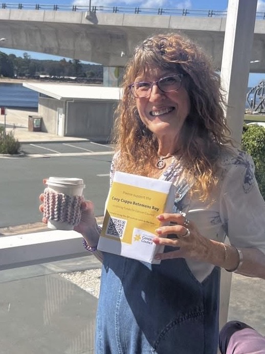 A photo of Sophie smiling with a flask in her right hand and a 'cosy cuppa batemans bay' donations box.
