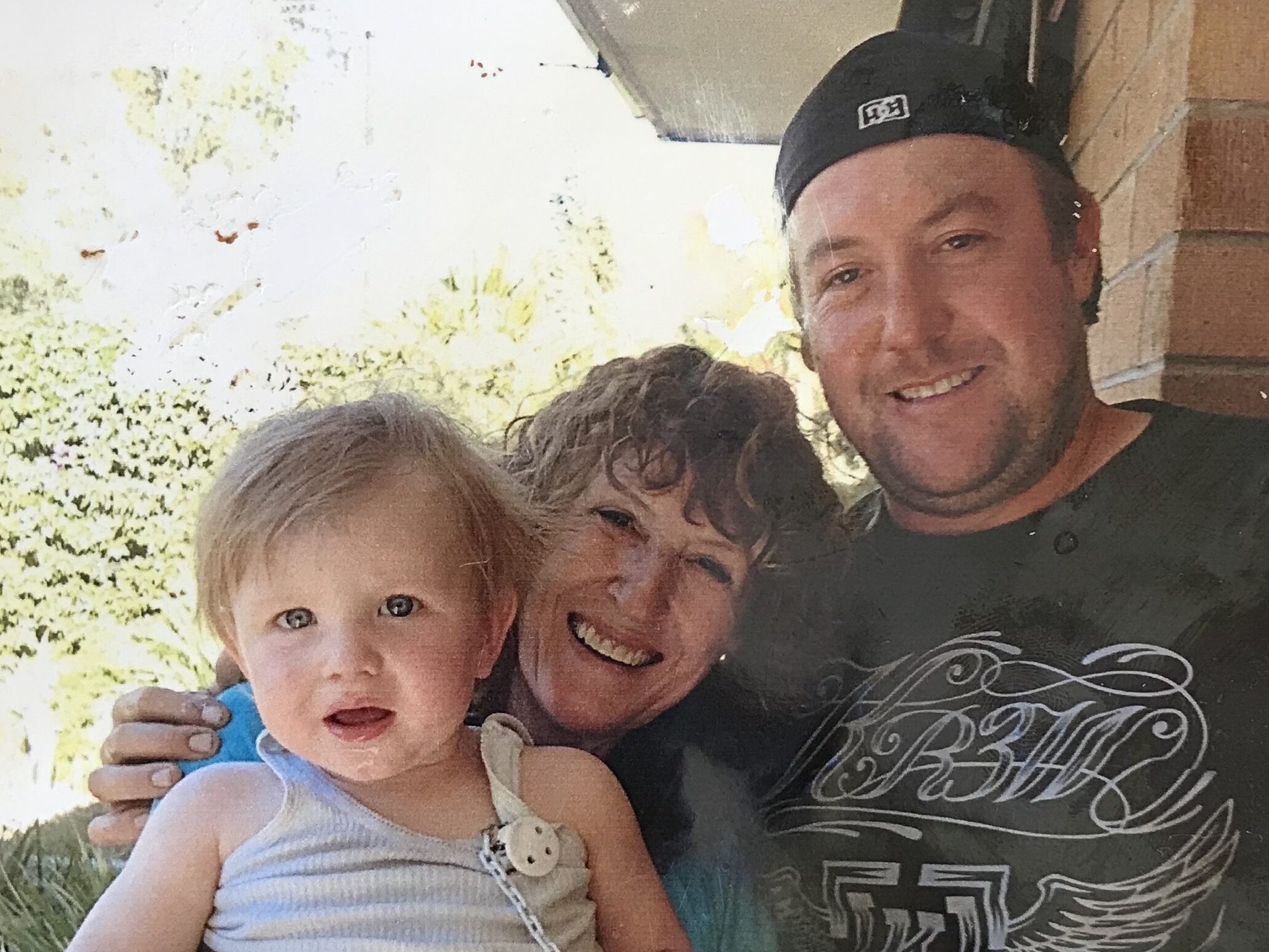 A photograph of smiling people. From left to right, Cole (Sophie's grandson), Sophie and Sam (Sophie's son).