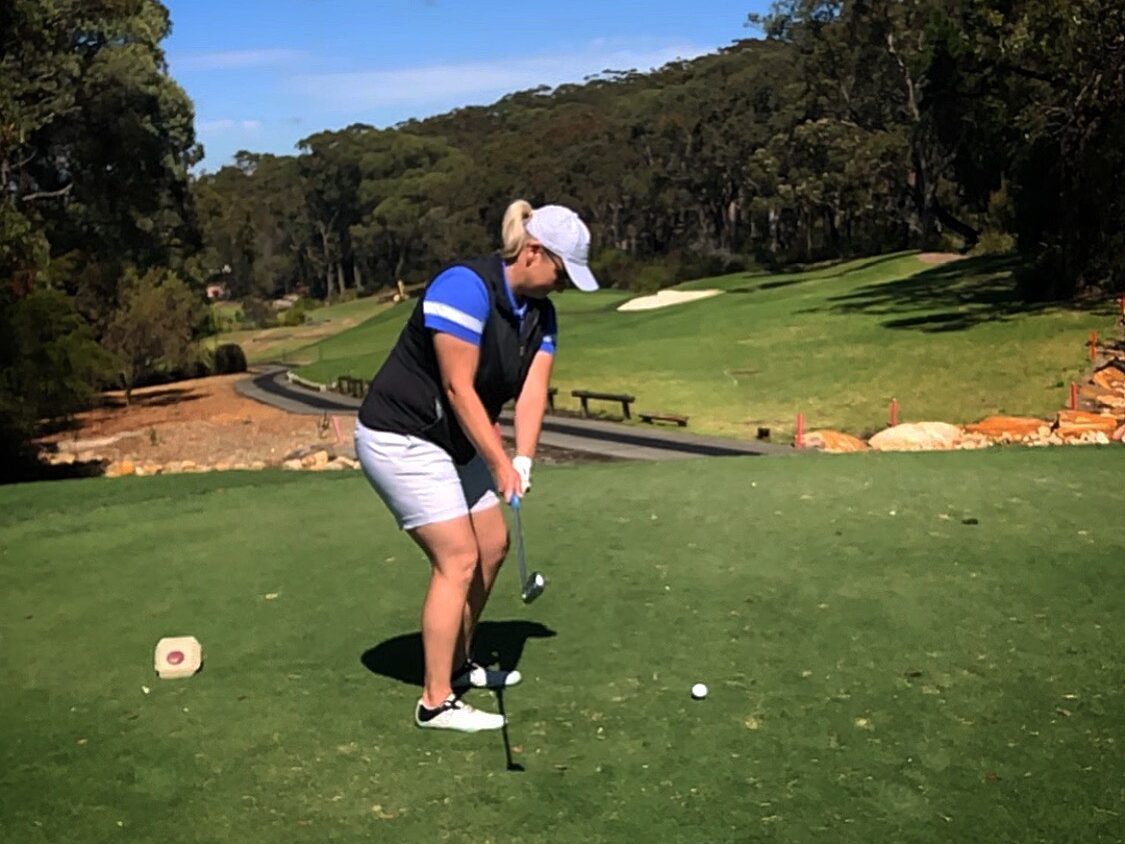 A picture of Jenny in her Sunsafe attire with a cap and sunglasses playing golf. 