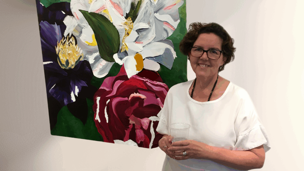 Here is a photo of Pam standing in front of a painting while holding a cup of water.