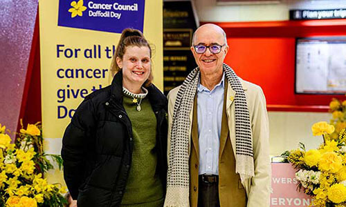 Two people stand in front of banners and daffodils